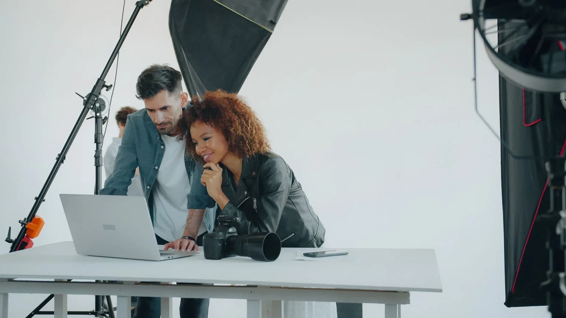 Two photographers reviewing work on a laptop in a professional studio setting.