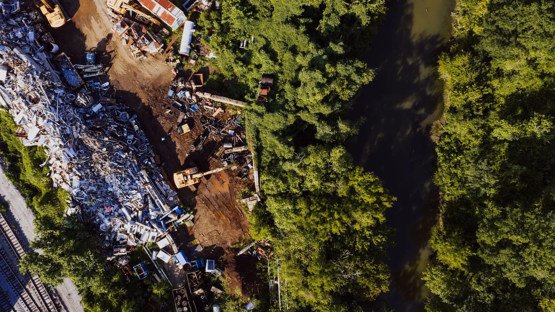 Aerial view of a junkyard adjacent to a river in Chattanooga, Tennessee, with lush summer greenery.