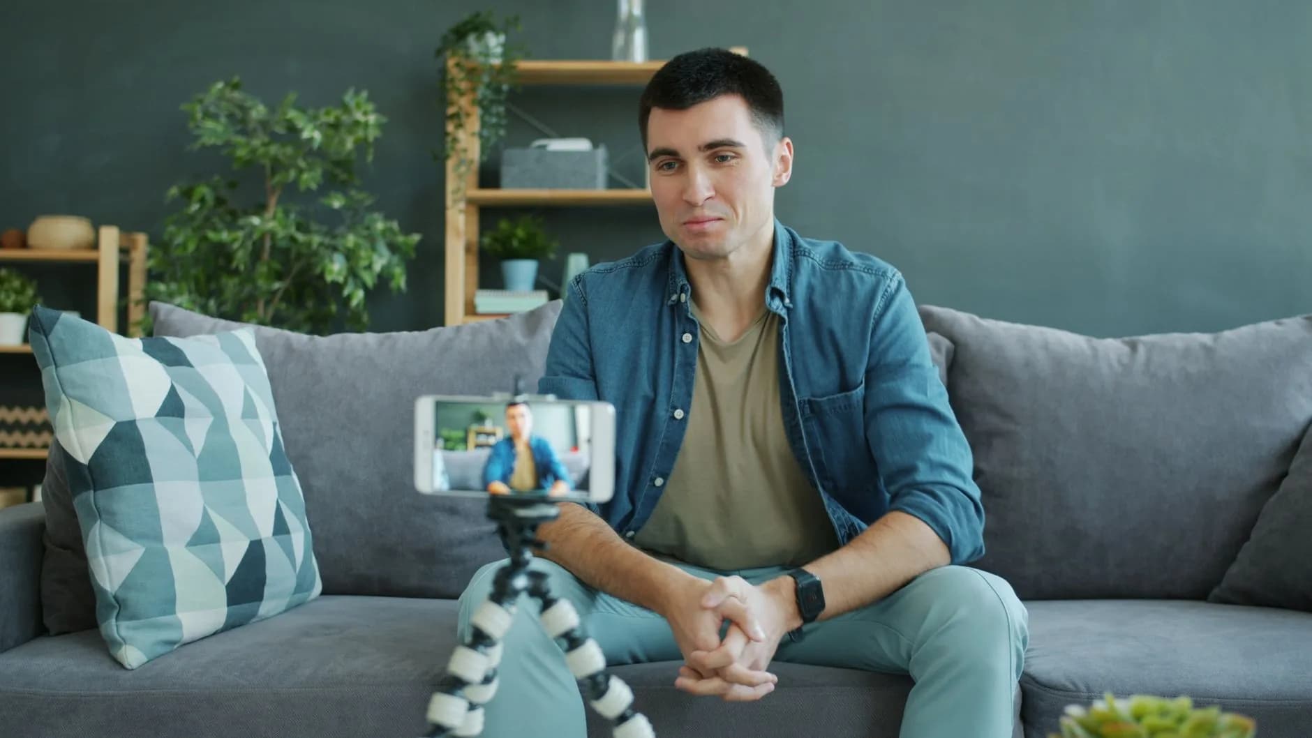 Young man filming himself at home using smartphone on tripod.