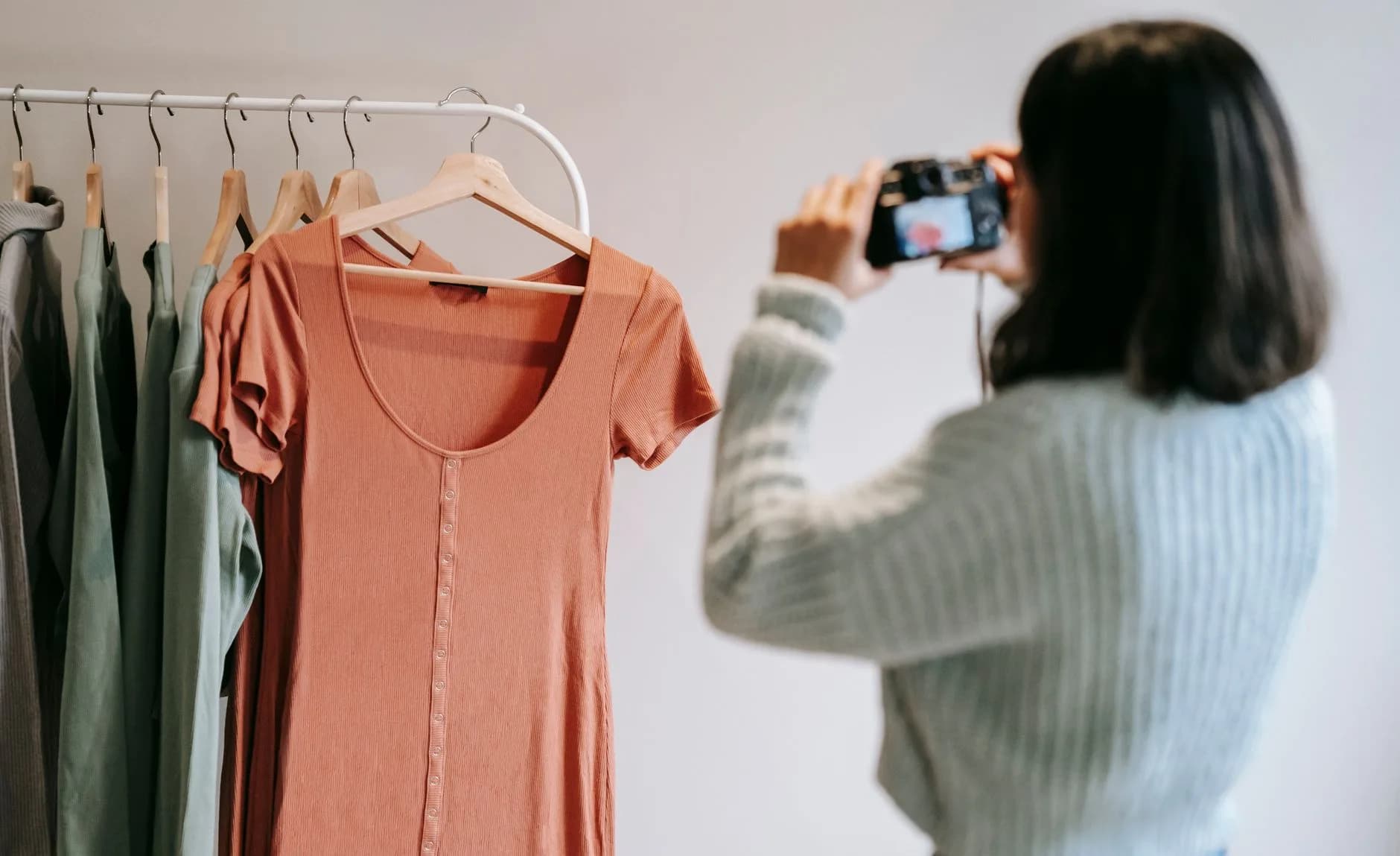 Back view of anonymous female taking photo of assorted wear on professional camera against rack