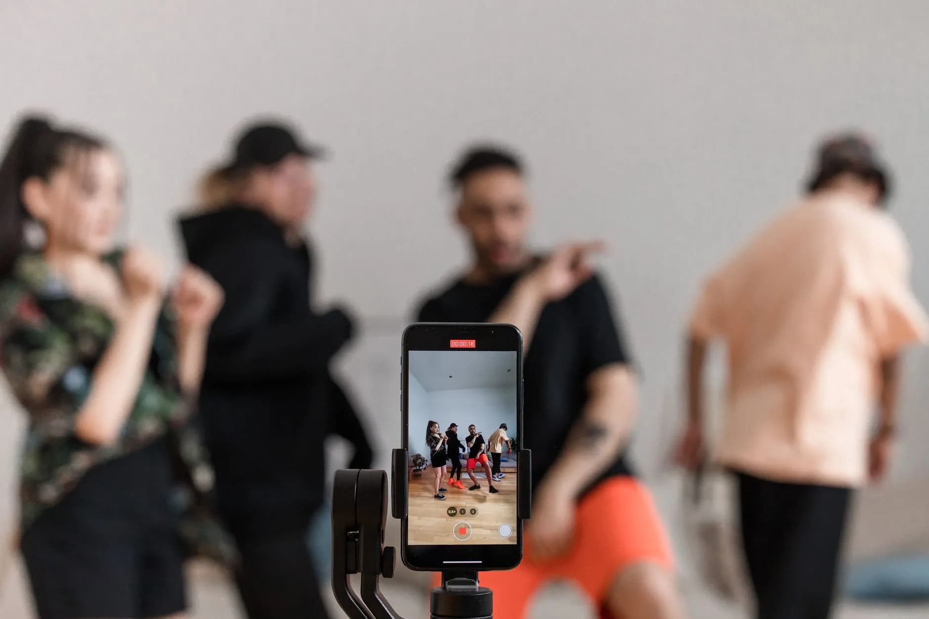 Group of dancers recording performance with smartphone on tripod, capturing trendy dance moves.